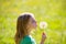 Blond kid girl blowing dandelion flower in green meadow
