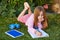 Blond kid girl homework lying on grass turf