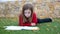 Blond kid girl maths homework laying on grass counting with fingers writing