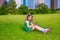 Blond kid girl playing with smartphone sitting on park lawn at c