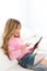 Blond kid girl playing with tablet pc on white sofa