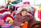 Blond kid girl sitting on a messy clothes sofa