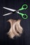 Blond lock of hair, metal open scissors black wooden background close up, cut off natural blonde hair curl on dark wood, shears