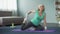 Blond middle-aged female doing stretching exercises on yoga mat at home, sport