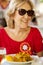 Blond older woman smiling and sitting at a table.