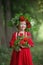 a blond preschool girl in a wreath of rowan and with toys walks in the park on a summer morning