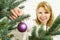 Blond pretty woman decorating christmas tree with purple ornaments decor balls.
