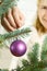 Blond pretty woman decorating christmas tree with purple ornaments decor balls.
