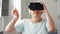 Blond senior woman in white using VR 360 glasses at home. Making browse, zoom and tap gestures