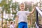 A blond seven-year-old boy in a white t-shirt and blue shorts looks at the camera on a blurred natural background