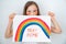 Blond teen girl drew rainbow and poster stay home.