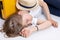 Blond teenage girl sleeping or resting near a yellow suitcase, a straw hat lies on it. Isolate on white