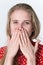 Blond woman covers mouth with hands, looking at camera. Authentic female in red polka dot dress