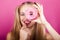 Blond woman looks through pink donut