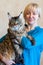 Blond woman, smiling, holds big and fluffy stunning cat of Maine Coon breed, with pretty face expression and green eyes.