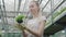 Blond young Caucasian woman smelling white flower in pot. Portrait of positive beautiful girl in apron and gloves