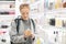 Blond young female traveler wearing travel backpack choosing perfume in airport duty free store.