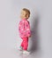 Blonde baby kid girl in pink warm fleece clothing with heart print pattern walks leaving out. Back view