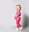 Blonde baby kid girl in pink warm fleece clothing with heart print pattern walks passes by camera. Side view