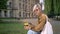 Blonde beautiful woman in sunglasses holding coffee and typing on phone, looking at camera, sitting in park near