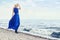 Blonde in blue dress walks along the promenade by sea, summer vacation at sea. Beautiful sensual portrait of a mysterious girl