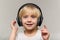 Blonde boy in headphones on light background. Child listens to music and smiles