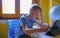 Blonde boy writing in copybook at the desk and looking into laptop. Educating, studying remotely, homeschooling. Online studying