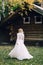 Blonde bride is walking in fluttering dress on wooden house background. Back view. Artwork