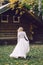 Blonde bride is walking in fluttering dress on wooden house background. Back view. Artwork