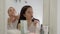 Blonde and brunette women are preening in front of mirror in room in morning time together, applying cream and painting