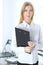 Blonde business woman standing straight and holding tablet in office background. Lawyer or secretary specialist at work