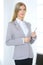 Blonde business woman standing straight and holding tablet in office background. Lawyer or secretary specialist at work