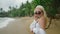 Blonde caucasian girl in sunglasses with straw hat by the sea looking at camera and smiling. Young happy female at beach