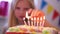 Blonde caucasian little girl lights candles on rainbow cake, makes a wish and blows them out at birthday party. Focus om
