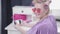 A blonde with curled hair is reviewing photos on a smartphone in pink glasses, turns her head and looks at the camera