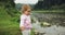 Blonde curly little girl throw stones in the river. Mountains background.
