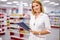 Blonde druggist woman in uniform checking the assortment in pharmacy
