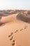 Blonde female Caucasian traveler leaving footprints in sand dunes when walking in dessert in Oman
