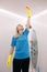 Blonde female cleaning pipe under ceiling in white shower cabin in bathroom