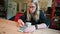 A blonde female with a stack of playing cards uses a smartphone while sat at a wooden kitchen table