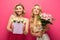 Blonde friends with bouquets smiling at camera on pink background