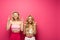 Blonde friends with crossed fingers on pink background