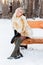 Blonde in fur coat, boots poses on wooden bench outdoor
