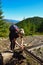 A blonde girl with a backpack drinks water from a homemade watering hole on the way to the top of the mountain