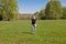 A blonde girl in a black T-shirt and jeans stands alone in a field against a background of green grass and trees and a blue sky in