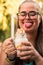 Blonde girl with glasses poses with her milkshake with cream and sticks out her tongue smiling