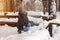 A blonde girl in a gray hat and a dark blue jacket in the winter in the forest is sitting in a snowdrift and throws her snow into