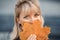 A blonde girl with green eyes hides behind a large maple leaf. Close up