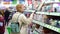 A blonde girl with a grocery basket in her hands walks around the store. A young girl walks around the supermarket