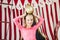Blonde girl holds golden ball on her head on circus decorations background